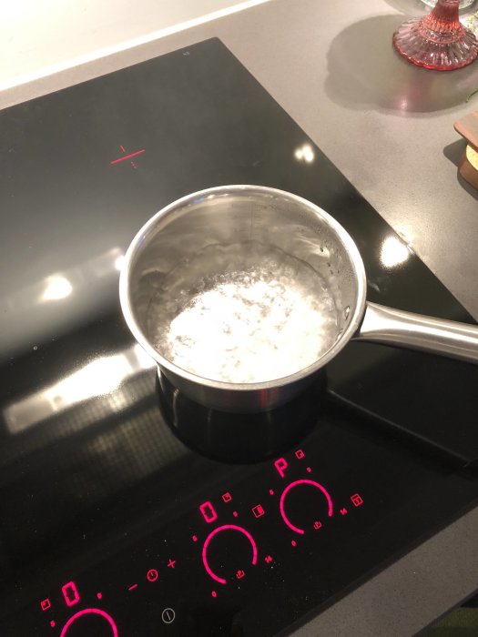 Kastrull med vatten nära kokpunkten på en induktionsspis med digitala kontroller som lyser rött.
