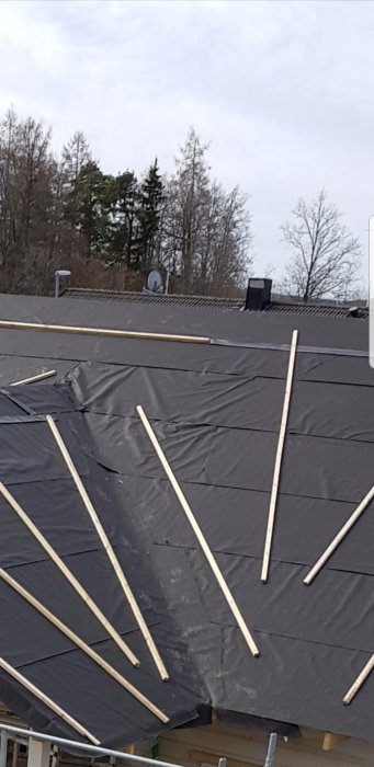 Tak under konstruktion med svart takduk och reglar på ett byggställningsskyddat hus.