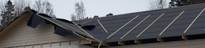 Solpaneler på ett hus med skadat tak där presenningar används för att täcka över hålen.