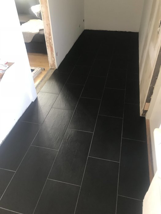 Nyligen rengjorda svarta klinkergolv i en halvfärdig hall, med öppet arbetsområde och material på golvet.