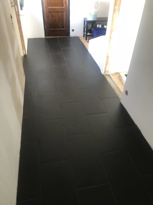 Renoverad hall med nytvättad mörk klinker och en synlig träddörr.