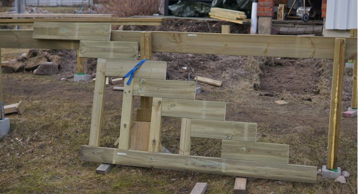 Nybyggd trävang på tomten, säkrad med spännband, provisorisk trappa och stenar i bakgrunden.