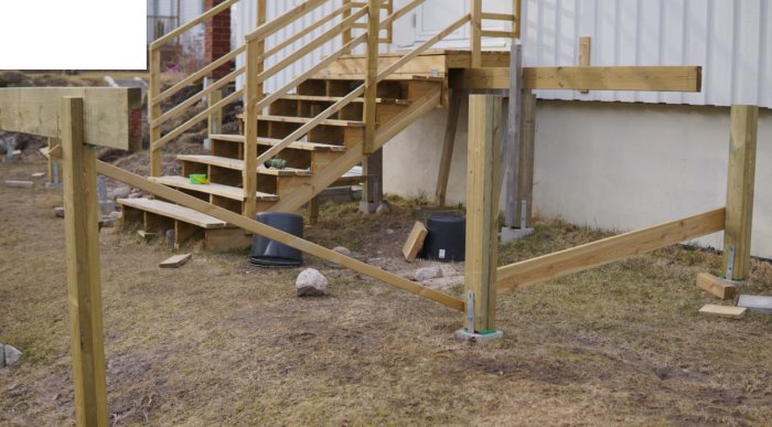 Nybyggd träram för altan med spännband, stenar staplade vid sidan och en provisorisk trätrappa i bakgrunden.