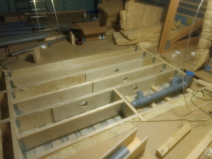 En pågående installation av avloppsrör på golvet i ett ofärdigt badrum på en övervåning, med synlig Uponor klosettböj och träbjälklag.