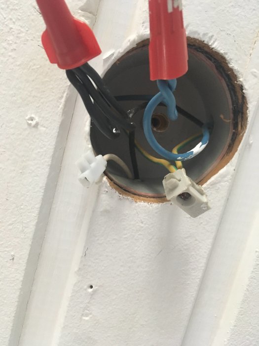 Öppen lampdosa i tak med synliga elektriska kablar och kopplingar som väntar på installation.