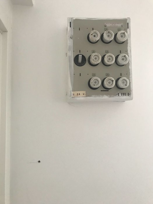 Ett öppet elskåp med säkringar på en vägg med en synlig hålighet till vänster om det.