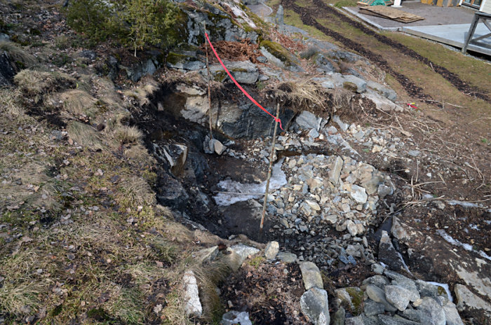 Sprängd bergsluttning med röd linje som markerar framtida takfotshöjd för växthusbygge.