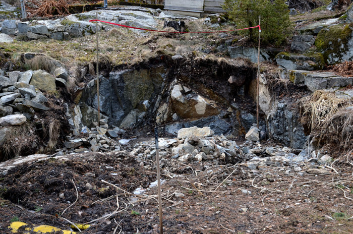 Bergsluttning med markerad höjd för takfot och mätpinnar för planerat växthusbygge.