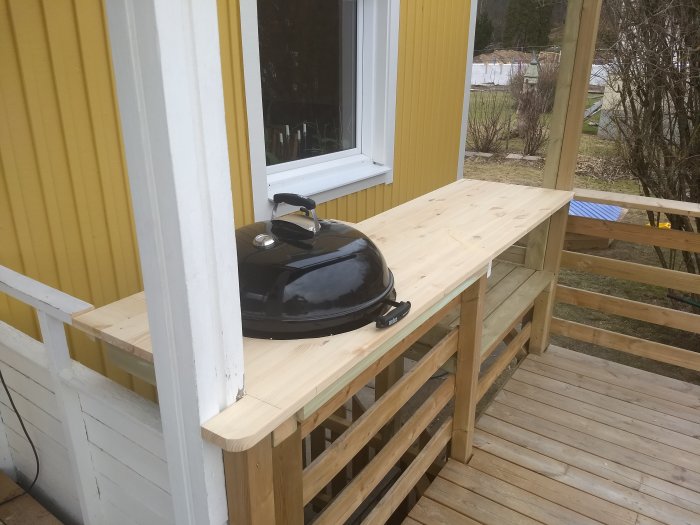 Nyinstallerad enkel trädgårdsbänkskiva utomhus vid gult hus, med en grill ovanpå.