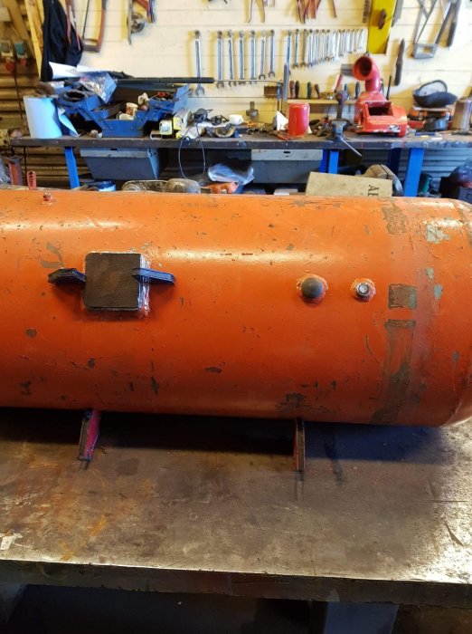 Orange gasoltank ombyggd till eldlåda med svetsade fästen i verkstadsmiljö.