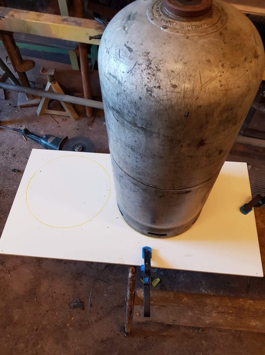 Trämall med utritad cirkel och stor metallbehållare på en vit arbetsbänk.