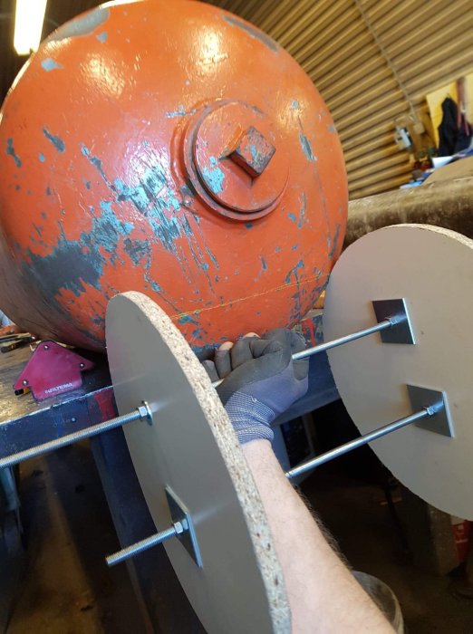 Person som håller i trämallar mot en rund orange yta för att märka ut en kurva.