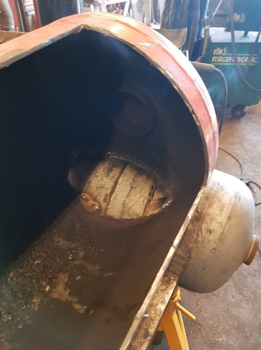 Ojämn och klumpig svetsfog på ett metallrör i en verkstad med svetsutrustning i bakgrunden.