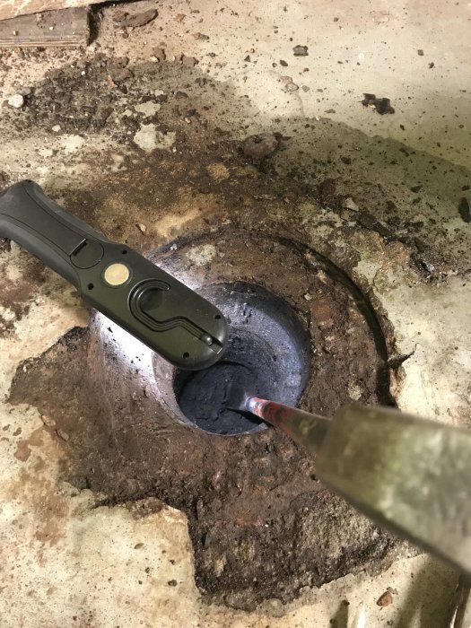 Igensatt avlopp med jord i ett garage, verktyg synligt vid öppningen.