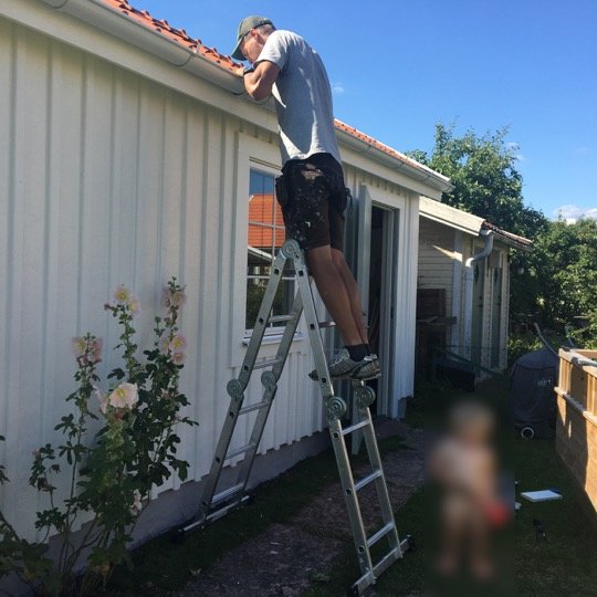 Person på stege arbetar med renovering av verkstadens fasad.