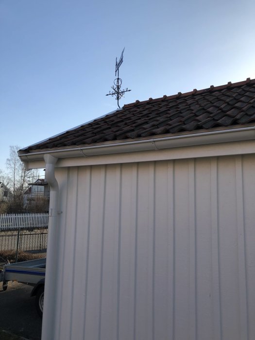 Nymålat garage i vit färg med ny vindflöjel på taket och renoverade takdetaljer mot en klar himmel.