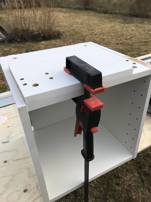 Modifierat IKEA högskåp med klämma fäst vid en kapad kant, utomhus på en gräsmatta.