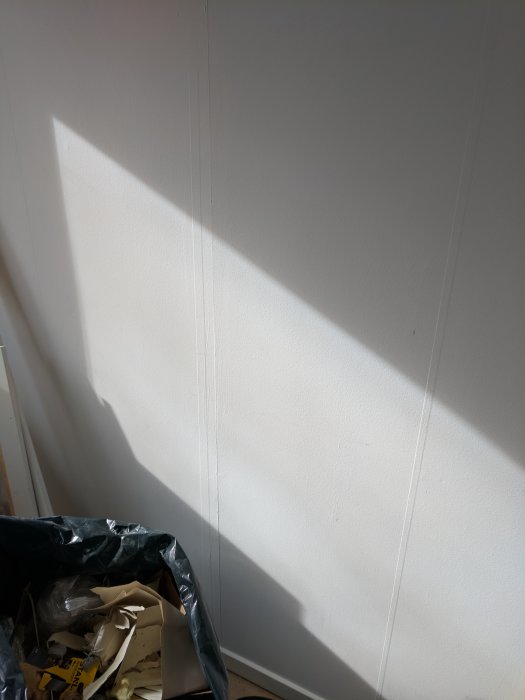 Vägg med synlig spricka mellan gipsskivor, ljusinsläpp och renoveringsavfall i förgrunden.