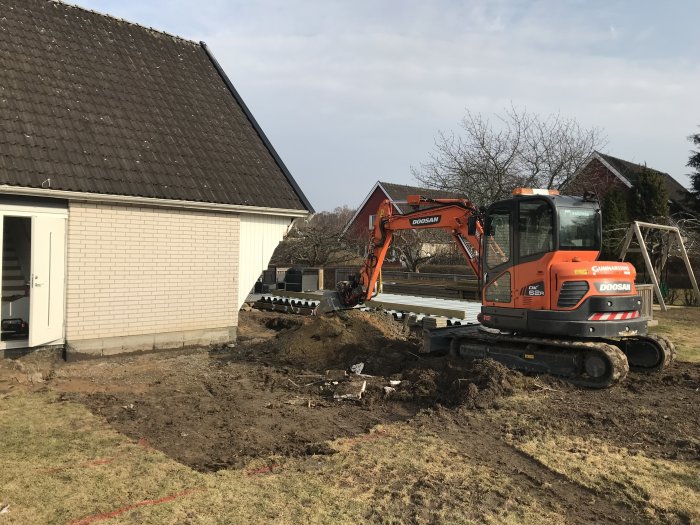 Grävmaskin vid arbete med att gräva för grund till uterum bredvid ett hus.