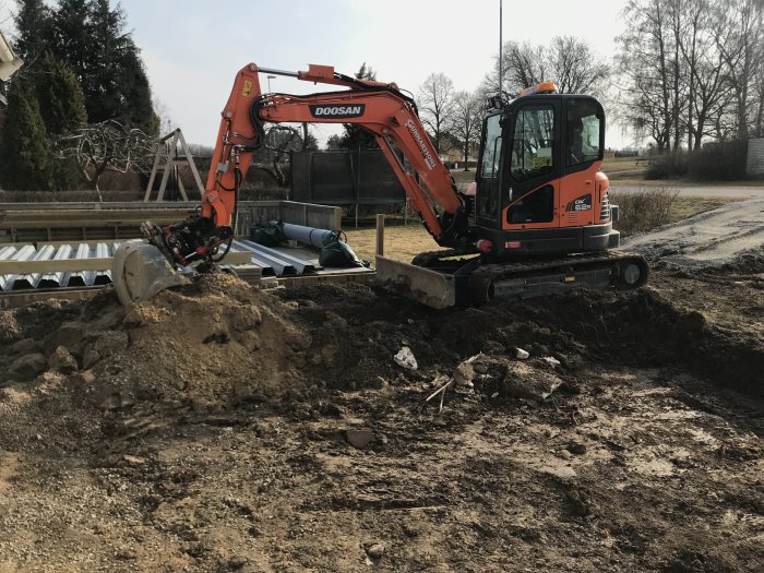 En orangefärgad grävmaskin Doosan på en byggarbetsplats, markerar starten för bygget av ett uterum.