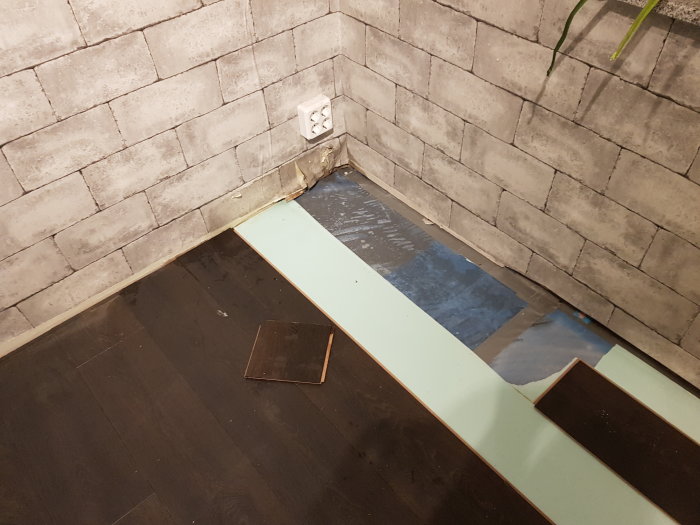 Vattenläckage under akvarium med upprivet laminatgolv och blött betonggolv vid vägg.