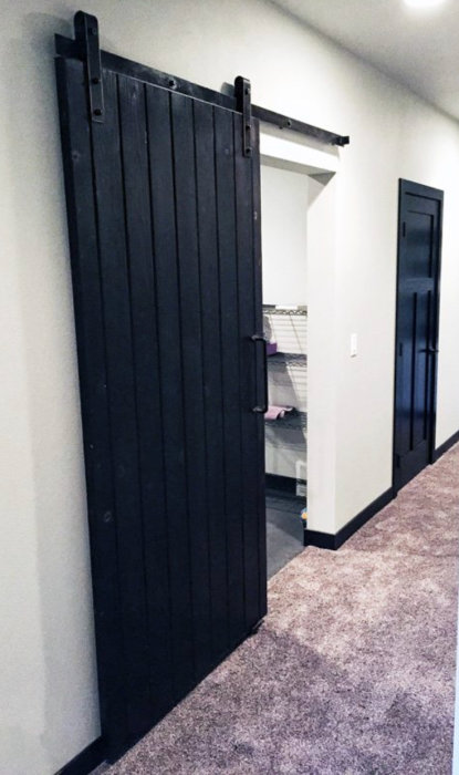 Svart "barndoor" skjutdörr på rullsystem öppnar mot ett torkskåp, inspirationsbild för hemrenovering.