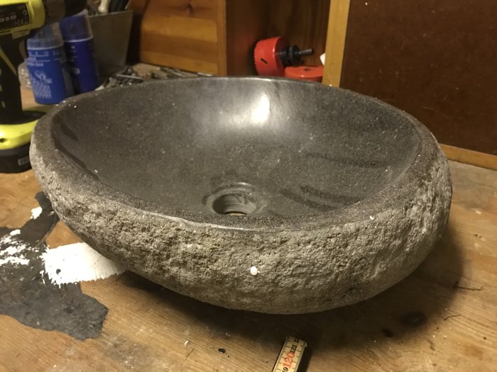 Ovalt handfat i natursten på ett trägolv, grov ytterkant med slät insida.