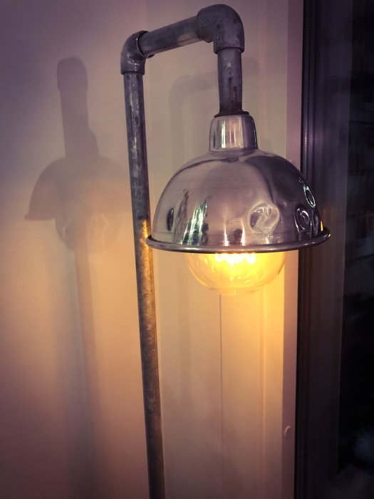 Närbild på en industriell designad vägglampa med en glänsande kupol och en synlig glödlampa.