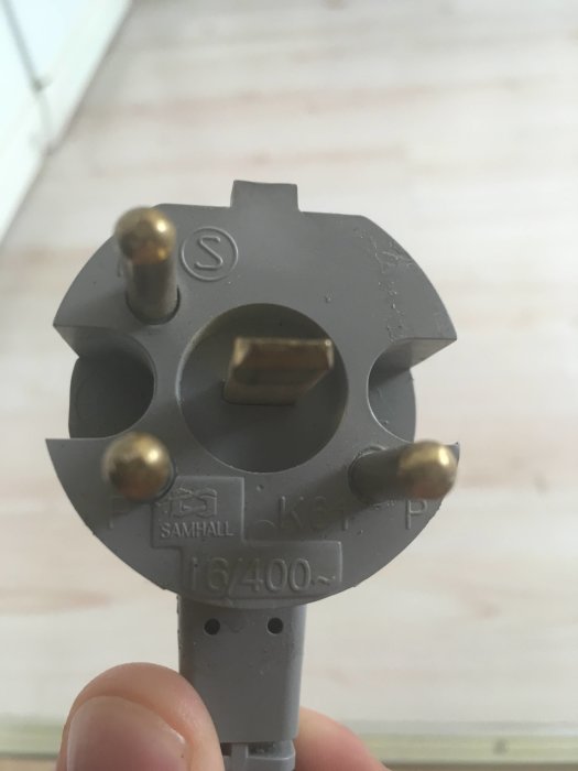 Hand som håller en grå stickpropp med tre poler och märkning "16A/400V", tänkt att användas för ugninstallation.