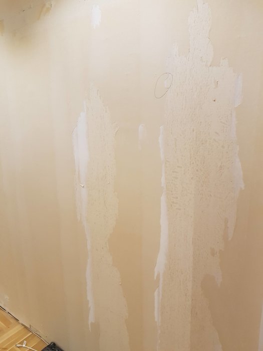 Vägg med bortriven vinyltapet som lämnat ojämna pappersrester och lösa våder.