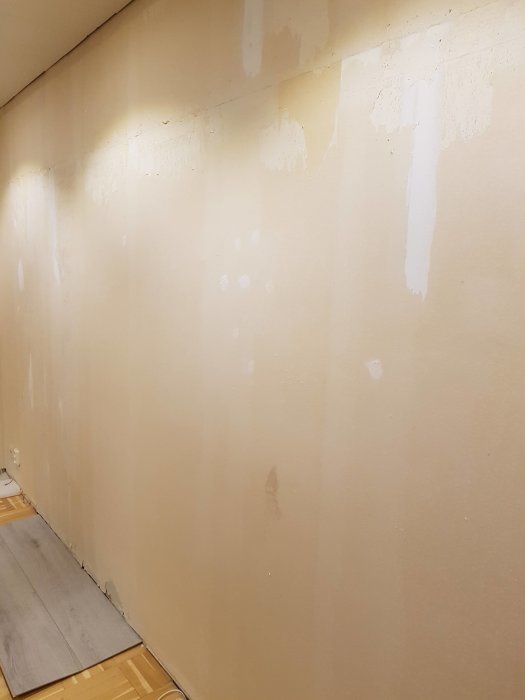 Vägg med rester av bortriven vinyltapet och vita limfläckar, redo för renovering.