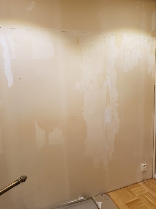 Vägg med ojämna pappersrester efter borttagning av vinyltapet, redo för renovering.