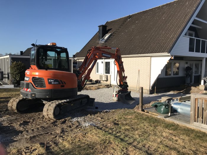 Grävskopa vid bostadshus med nylagt dräneringsrör och singel för återfyllning och paddning.