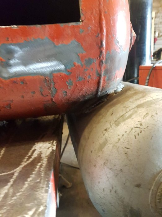 Svetsad eldlåda i metall med synliga svetsfogar och slitage på röd färg.