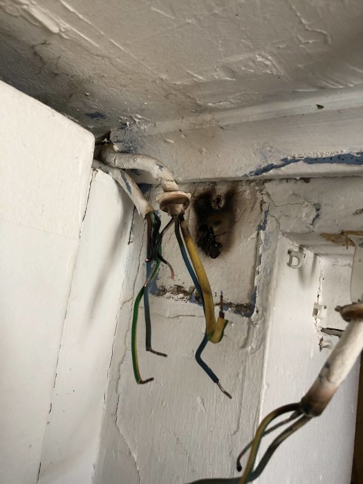 Gammal elinstallation med synliga kopplingsplintar och oskyddade elkablar i en oöppnad väggdosa.