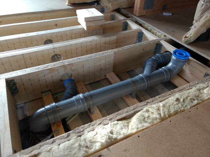 Avloppsrör med böjar installerade mellan golvbjälkar, sticker upp ovanför bjälkarna.