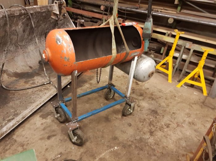 En orange tunna på ett blått hjulställ i en verkstad, upphängd och redo att anpassas till benkonstruktionen.