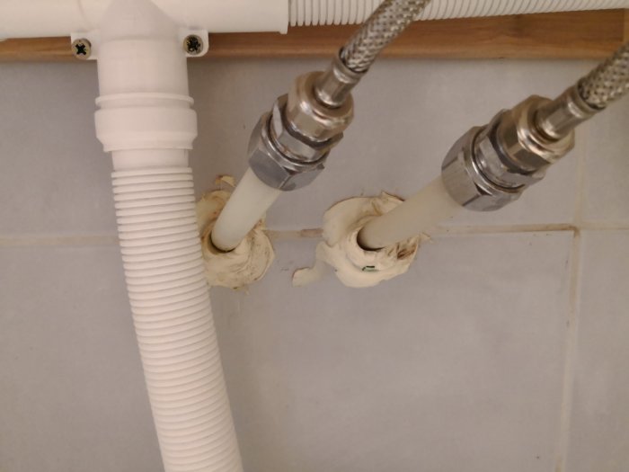 Pex-rör sticker ut ur väggen genom tätningsmaterial, ansatt mot flexibla metallslangar, behöver kapas för ny badrumsmöbel.