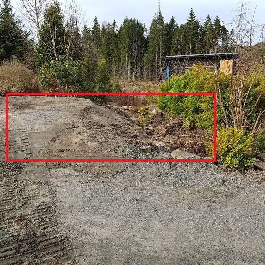 Uppgrävd tomt markerad för anläggning av parkeringsplats med varierande höjd och vegetation i bakgrunden.