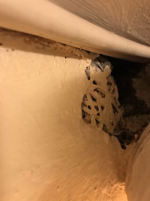 Rutnätsmaterial synligt innanför en källargrund i ett hus, delvis dolt av vitputsade ytor.
