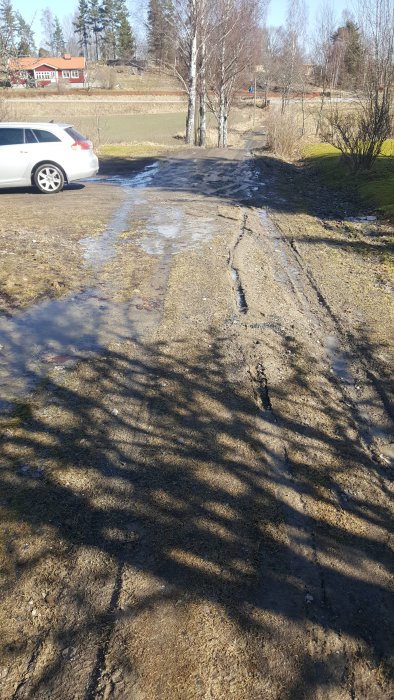 Eroderad grusväg med spår efter avgrävda dräneringsrör och vattensamlingar.