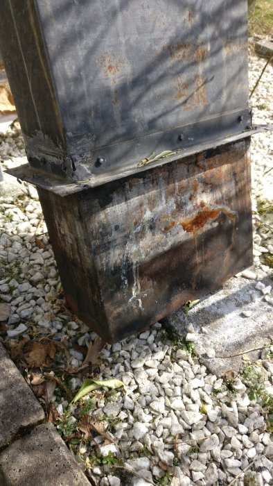 Rostig skorstenshuva som ligger på grusmark redo att monteras på murad skorsten.