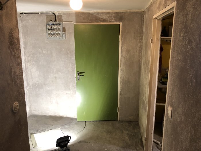 Renoveringsprojekt med slätputsväggar klara för målning, spacklat golv runt rör, grön dörr utan foder.