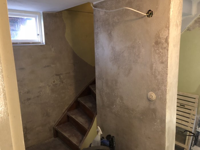 Renoveringsarbete med putsade och spacklade väggar samt en trätrappa i ett bostadsrum.