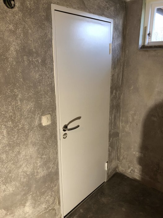 Renoverat rum med putsade väggar och en vit dörr utan foder, redo för målning.