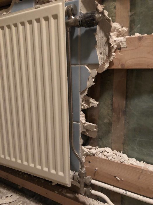 Radiator bredvid rivet badrumsvägg, med synlig umbrakoskruv vid kopplingen.
