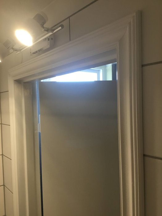 Dörrkarm vid kakelvägg med synlig limsträng och klämma för att minska glipan.