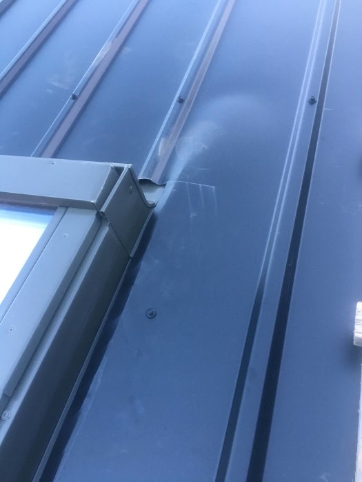 Närbild av ett nyinstallerat takfönster med metallplåt och en korrugerad skiva vid kanten.