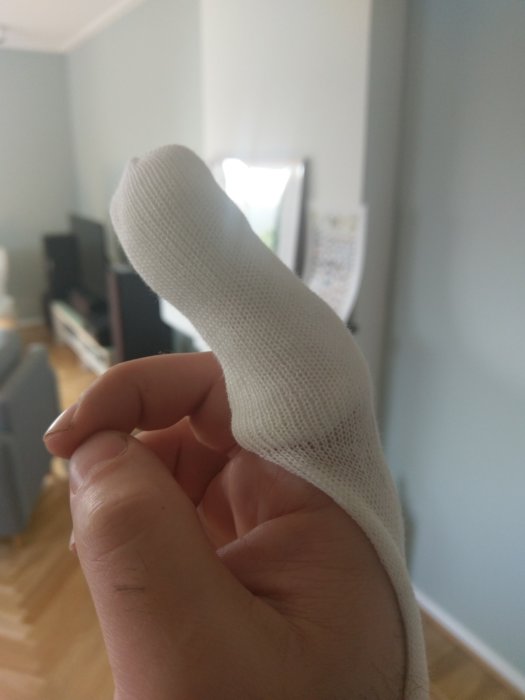 Person som håller upp sin skadade finger insvept i ett bandage efter en olycka med en såg.