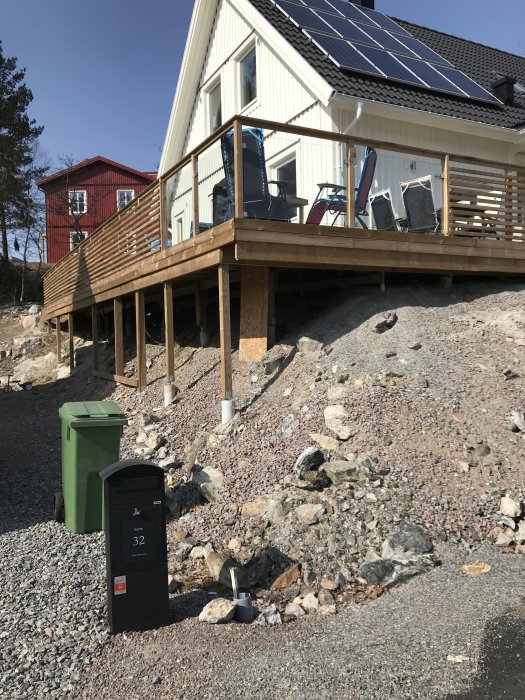 Trädäck med räcke och solpaneler på taket av ett vitt hus, grannhus i bakgrunden.